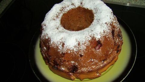 Ein Vanille-Napfkuchen auf einem Teller, garniert mit Puderzucker, steht auf einer dunklen Arbeitsfläche.