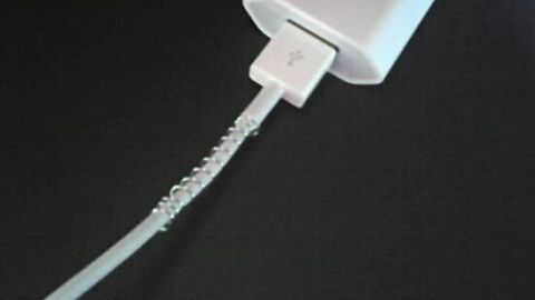 Ein Ladekabel mit Spiralfeder umwickelt, verhindert Kabelbruch beim Anschluss an ein weißes Ladegerät auf schwarzem Untergrund.