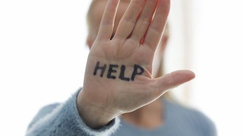 Eine Hand mit der Aufschrift "HELP" zeigt nach vorn, während eine Person im Hintergrund unscharf bleibt, um Hilfe zu signalisieren.