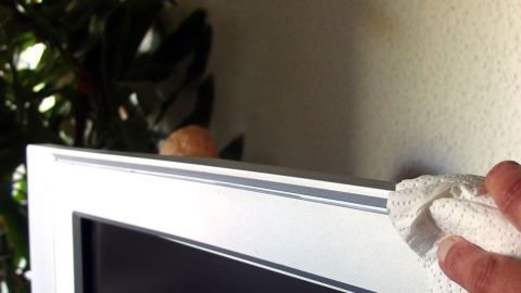 Edding von Möbeln & glatten Oberflächen entfernen mit Autopolitur. Ein Handtuch wischt die Kante eines Fernsehers ab, um Edding und Schmutz von glatten Oberflächen zu entfernen.