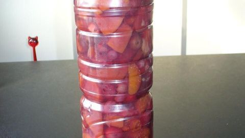 Ein Durchsichtiger Behälter mit Früchten für Sangria, gefroren und aufrecht auf einer dunklen Oberfläche stehend.