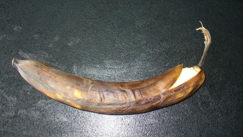 Eine überreife Banane liegt still auf einer dunklen Oberfläche, ihre Schale teils geöffnet, zeigt die gelbe Frucht.