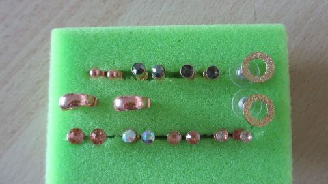 Ohrstecker sind ordentlich auf grüner Schaumstoffplatte befestigt; glänzende Designs in verschiedenen Formen und Farben.