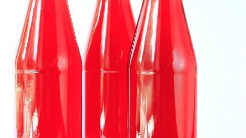 Drei Glasflaschen mit rotem Erdbeerwein stehen auf einem weißen Hintergrund, dekoriert mit karierten Deckeln.
