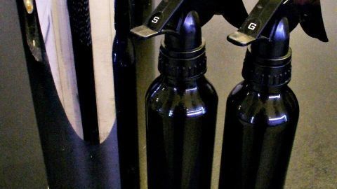 Schwarze Sprühflaschen stehen neben einem glänzenden, durchlöcherten Behälter auf einem dunklen Tisch.