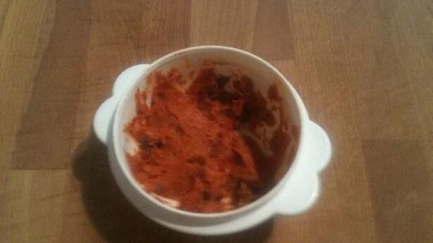 In einer weißen Schüssel ruht Tomatenbutter, halb verbraucht, auf einem Holztisch, bereit zum Genießen.