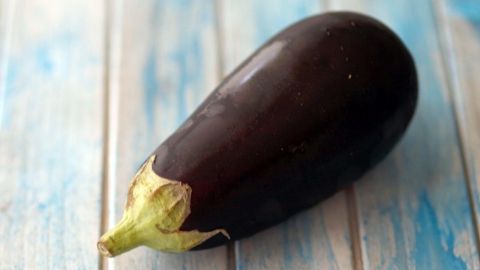 Eine glänzende Aubergine liegt auf einer hellblauen, holzähnlichen Oberfläche, bereit zum Kochen in der Mikrowelle.