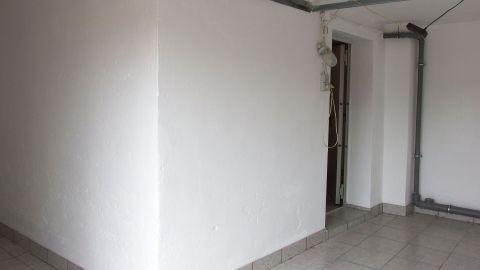 Eine weiße Wand mit kleinen Macken steht im Fokus, zu reparieren in einem hellen Raum mit Fliesenboden.