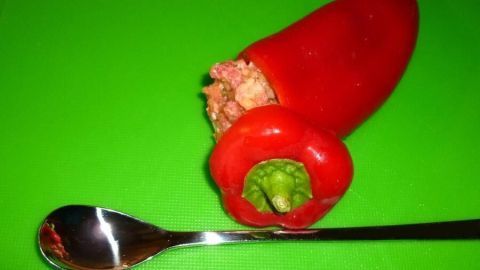Gefüllte rote Spitzpaprika liegt auf grünem Schneidebrett mit einem Esslöffel daneben, gefüllt mit würzigem Hackfleisch.