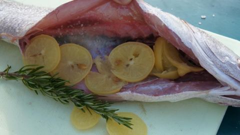 Ein gefüllter Fisch liegt auf einem Schneidebrett, mit eingelegten Zitronen und Gewürzen im Inneren, bereit zum Kochen.
