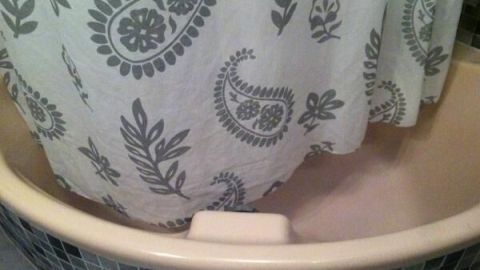 Ein Duschvorhang mit floralem Muster hängt in einer Badewanne, umgeben von dunklen Fliesen.