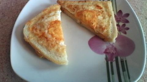 Eine Scheibe Käse-Ei-Toast liegt in zwei Hälften geschnitten auf einem Teller mit Blumenmuster auf einer Küchenarbeitsplatte.