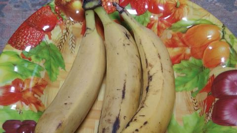 Drei Bananen liegen auf einem bunten Teller mit Obstmotiv, während sie reif werden und bereit zum Einkaufen sind.