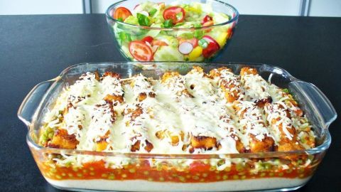 Ein frisch gebackener Fischstäbchen Auflauf liegt in einer Glasform, umgeben von einer bunten Salatschüssel.