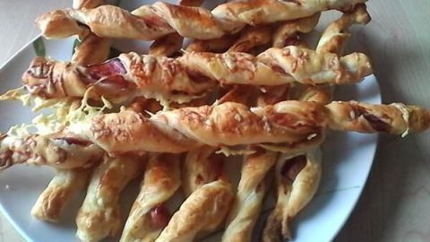Blätterteigstangen sind knusprig und goldbraun, auf einem weißen Teller liegen sie verführerisch und duften nach Käse.