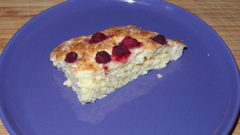 Ein Hefekuchenstück liegt auf einem blauen Teller, mit Himbeeren belegt, und wartet auf den Genuss.