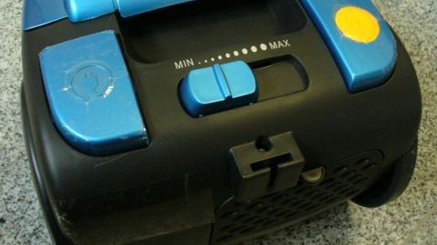 Staubsauger mit blauer Steuerung auf grauem Boden, zeigt Regler für "MIN...MAX".