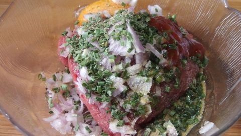 Frikadellen- oder Hackbraten-Masse liegt in einer Schüssel, gewürzt mit Kräutern und Zwiebeln, bereit zum Formen.