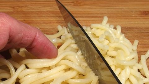 Spaghetti werden mit einem Messer auf einem Holzbrett in kleinere Stücke geschnitten, um Reste sinnvoll zu verwerten.