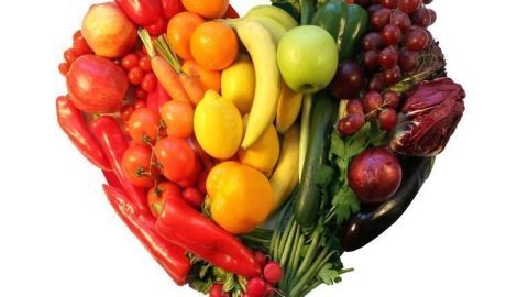 Obst und Gemüse formen ein Herz, bunt arrangiert auf weißem Hintergrund, symbolisieren eine vegetarische Ernährung.