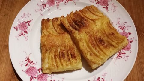 Zwei goldbraune Stücke Apfelkuchen vom Blech liegen auf einem dekorativen Teller in einer warmen Küchenumgebung.