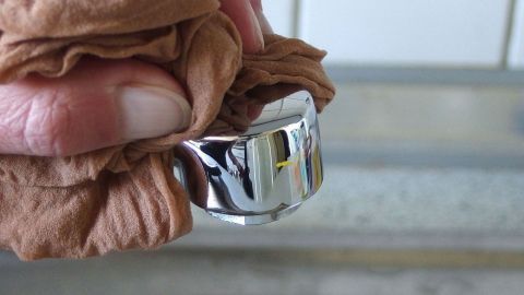 Ein glänzender Wasserhahn wird mit einem Tuch gereinigt, während sich eine Spüle im Hintergrund befindet. Armaturen polieren ohne Chemie.