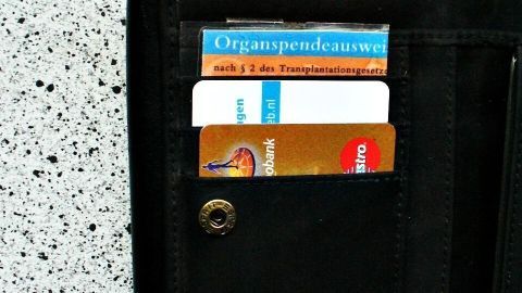 Eine schwarze Geldbörse zeigt einen Organspendeausweis und diverse Karten. Daneben liegt ein Schlüsselanhänger auf hellem Tisch.