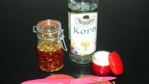Chili und Messer auf rotem Brett, Glas mit eingelegtem Chili und Flasche Altstädter Korn daneben auf schwarzem Tisch.