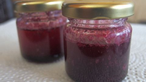 Zwei kleine Gläser mit Holunderbeeren-Butter stehen auf einem Tisch und zeigen eine tiefrote, süße Konsistenz.
