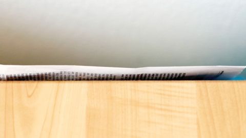 Bewahre Sauberkeit über deinem Küchenschrank: Lege Zeitungspapier aus, um Fett und Staub abzufangen. Wechsel einfach das Papier, und deine Küche bleibt mühelos ordentlich und gepflegt. Ein dünnes Blatt Papier liegt flach auf einem Küchenschrank, Text ist teilweise sichtbar und Hintergrund ist unscharf.