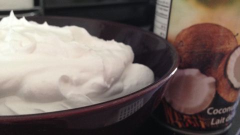 Eine Schüssel mit aufgeschlagener Kokosmilch steht neben einer Dose mit Kokosnuss. Die Sahne ist fluffig und weiß.