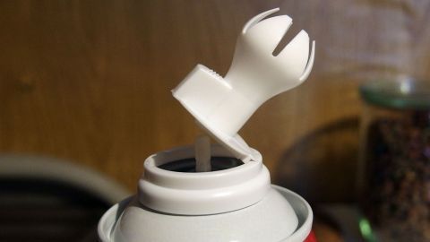 Eine Sprühsahne-Dose steht geöffnet auf einem Tisch, bereit zum Sprühen, während im Hintergrund eine warme Holzstruktur sichtbar ist.