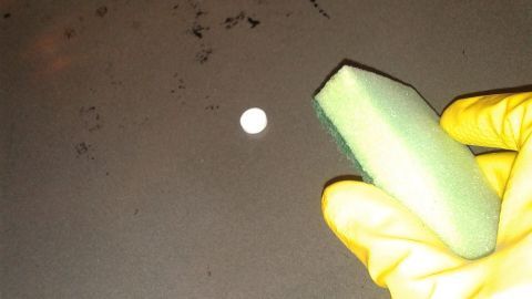 Eine gelb behandschuhte Hand hält einen Schwamm, um Verkrustungen im Backofen auf einer schmutzigen Oberfläche zu entfernen.