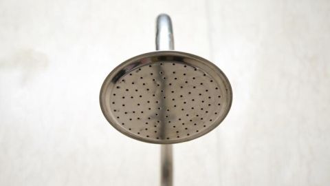 Duschkopf sprüht Wasser senkrecht in einem hellen Badezimmer; ideal für Duschkabinen-Reiniger.