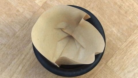 Ein Kaffeefilter liegt in einem Blumentopf und ersetzt die Tonscherbe, um das Gießen zu erleichtern.