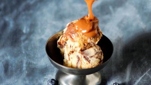 Karamellsoße wird über eine Kugel Eis in einer metallenen Schüssel gegossen, um das Dessert zu verfeinern.