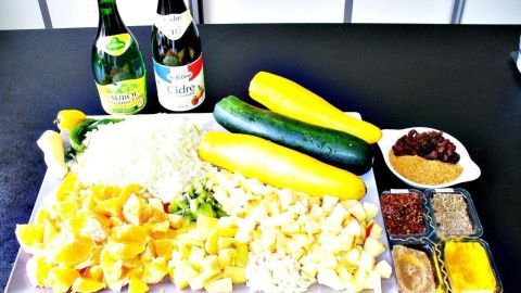 Eine große Platte zeigt frisch gewürfelte Zucchini, Äpfel und Zwiebeln, neben Essigflaschen und Gewürzen zum Chutney.