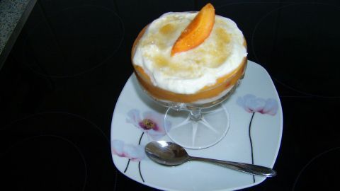 Eine Dessertschale mit Mascarpone-Creme und Aprikosenstück, angerichtet auf einem Teller mit Löffel, steht auf einem Herd. Text: "23/07/2014 12:04".
