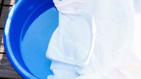Ein weißes T-Shirt liegt in einem blauen Waschbehälter, eingetaucht in klares Wasser zur Fleckenentfernung.
