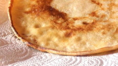 Ein goldbrauner Pfannkuchen liegt auf einem weißen Papiertuch und zeigt seine leicht knusprige Textur.