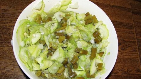 Ein frischer Zucchini-Gurken-Bohnensalat in einer weißen Schüssel wird auf einem Holztischtuch serviert.