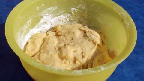 Ein gelbes Schüssel mit Hefeteig lässt in der Sonne gehen; der Teig ist leicht klebrig und umgeben von etwas Mehl.