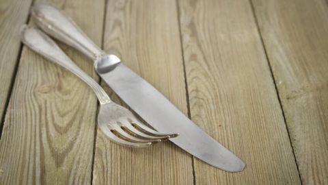 Besteck liegt auf Holztisch, ein silbernes Messer und eine Gabel bilden eine ruhige, nostalgische Komposition.