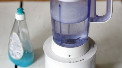 Ein Standmixer steht auf einem weißen Tisch, während eine Flasche Geschirrspülmittel daneben platziert ist.