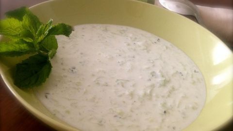 In einer gelben Schüssel liegt eine kalte türkische Gurkensuppe, die cremig und frisch aussieht, mit einem Minzblatt dekoriert.