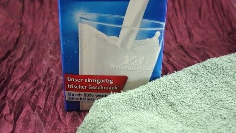 Eine Milchpackung wird in ein Glas gegossen, während ein grünes Handtuch im Vordergrund liegt, passend zur Hilfe bei Sonnenbrand.