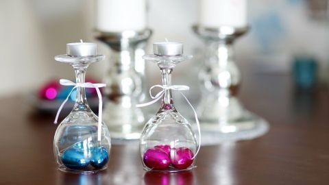 Farbenfrohe Tischdeko mit kleinen Glasgefäßen, die mit blauen und pinken Kugeln gefüllt sind, neben stilvollen Kerzenhaltern.