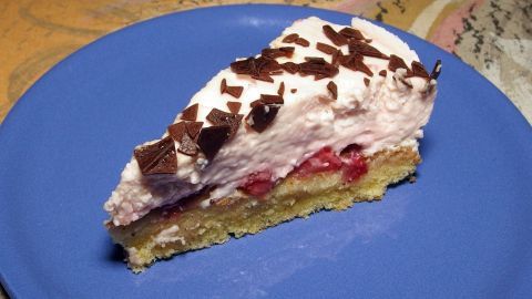 Ein Stück Kuchen auf einem blauen Teller, dekoriert mit Sahne und Schokoladenstückchen, steht auf einem holzfarbenen Tisch.