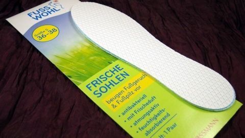 Weiße Einlegesohle liegt auf einer grünen Verpackung, die frische Füße bei heißem Wetter verspricht und auf Komfort hinweist.