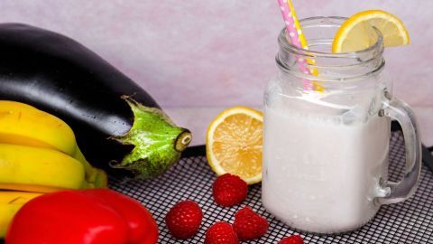 Ein Glas gesunder Cocktail mit einer gelben Zitrone und einem bunten Strohhalm steht neben frischen Früchten und Gemüse.